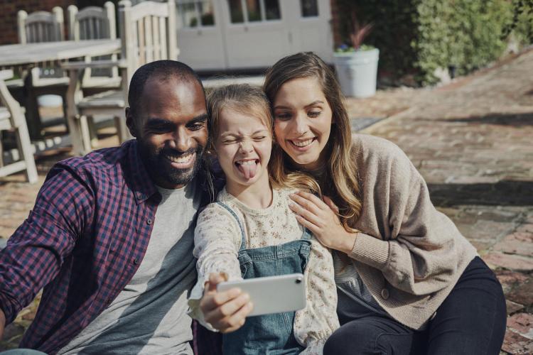 Young girl holding up a phone to take a photo with her parents